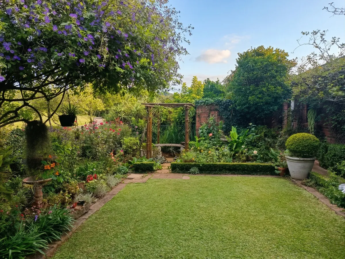 A beautifully landscaped garden in Howick featuring a pristine lawn, vibrant flowering plants, and a custom rustic wooden archway.