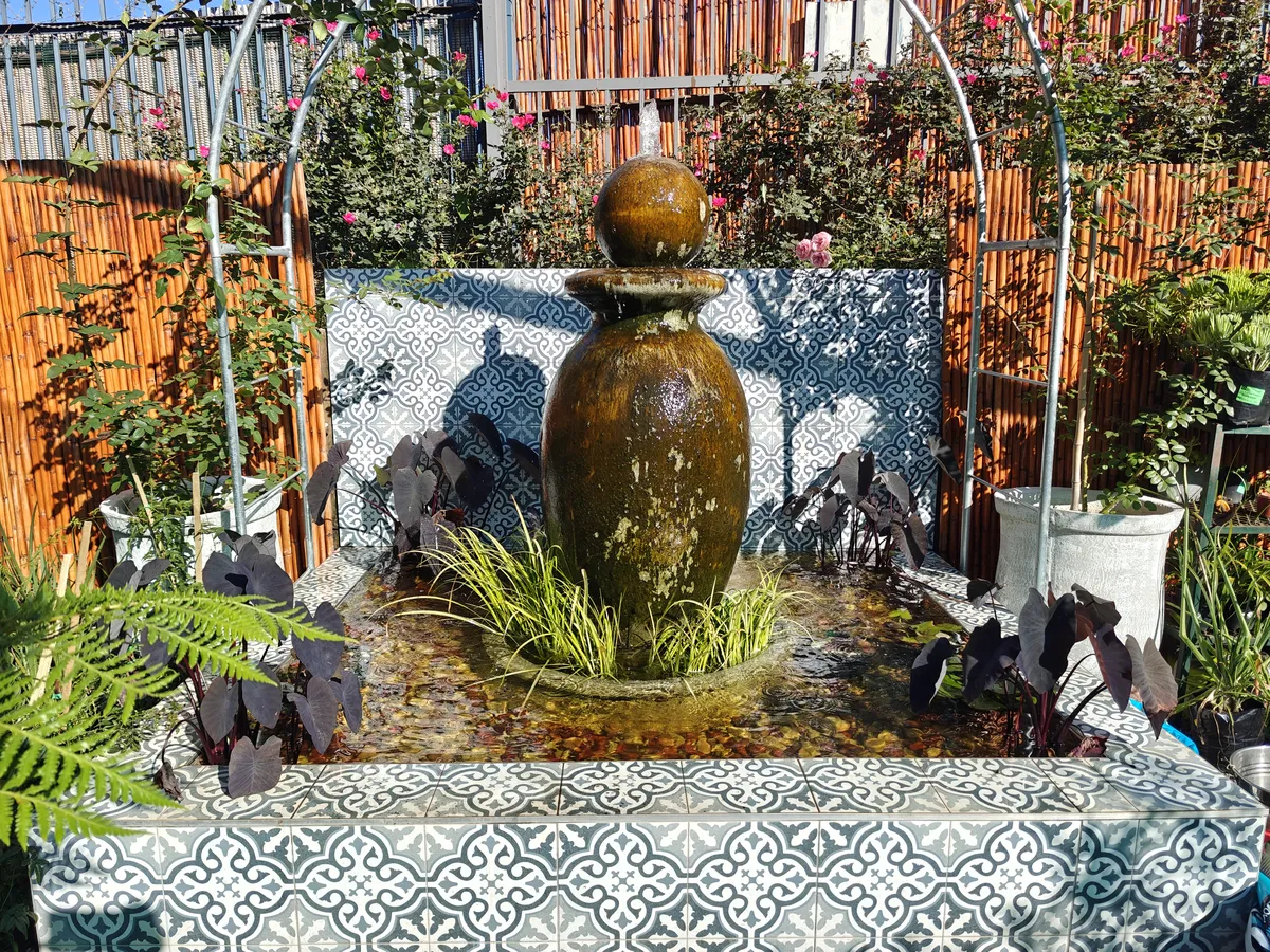 A custom water feature with a glazed urn fountain surrounded by aquatic plants, set in a raised pond clad in patterned Moroccan-style tiles.
